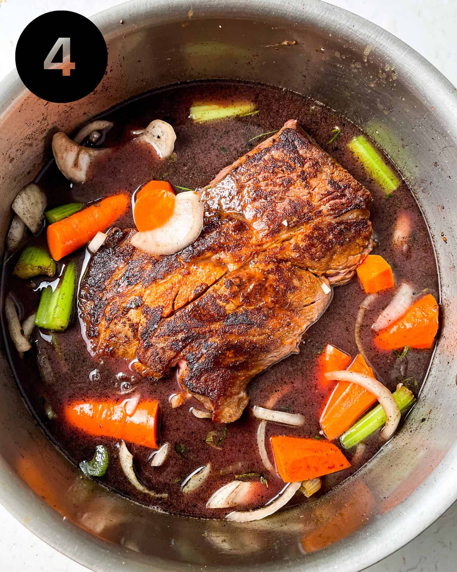 chuck roast in a pan with braising liquid and veggies.