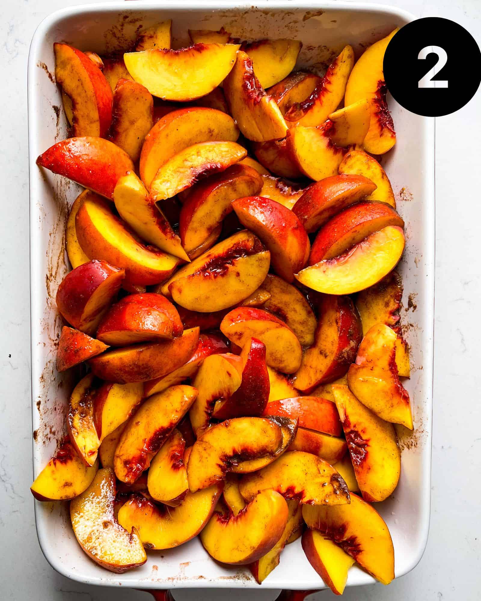 yellow peaches tossed in sugar and spices in a 9x13 baking dish.