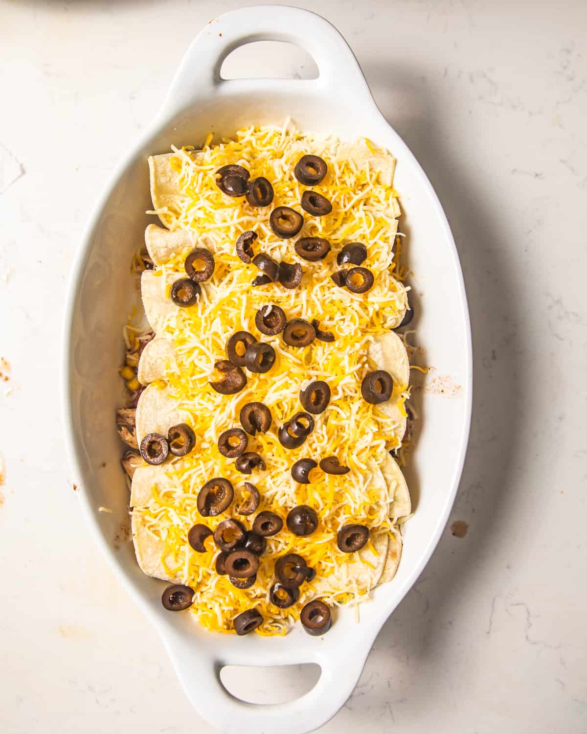 chicken enchiladas in a casserole dish topped with cheese and olives.