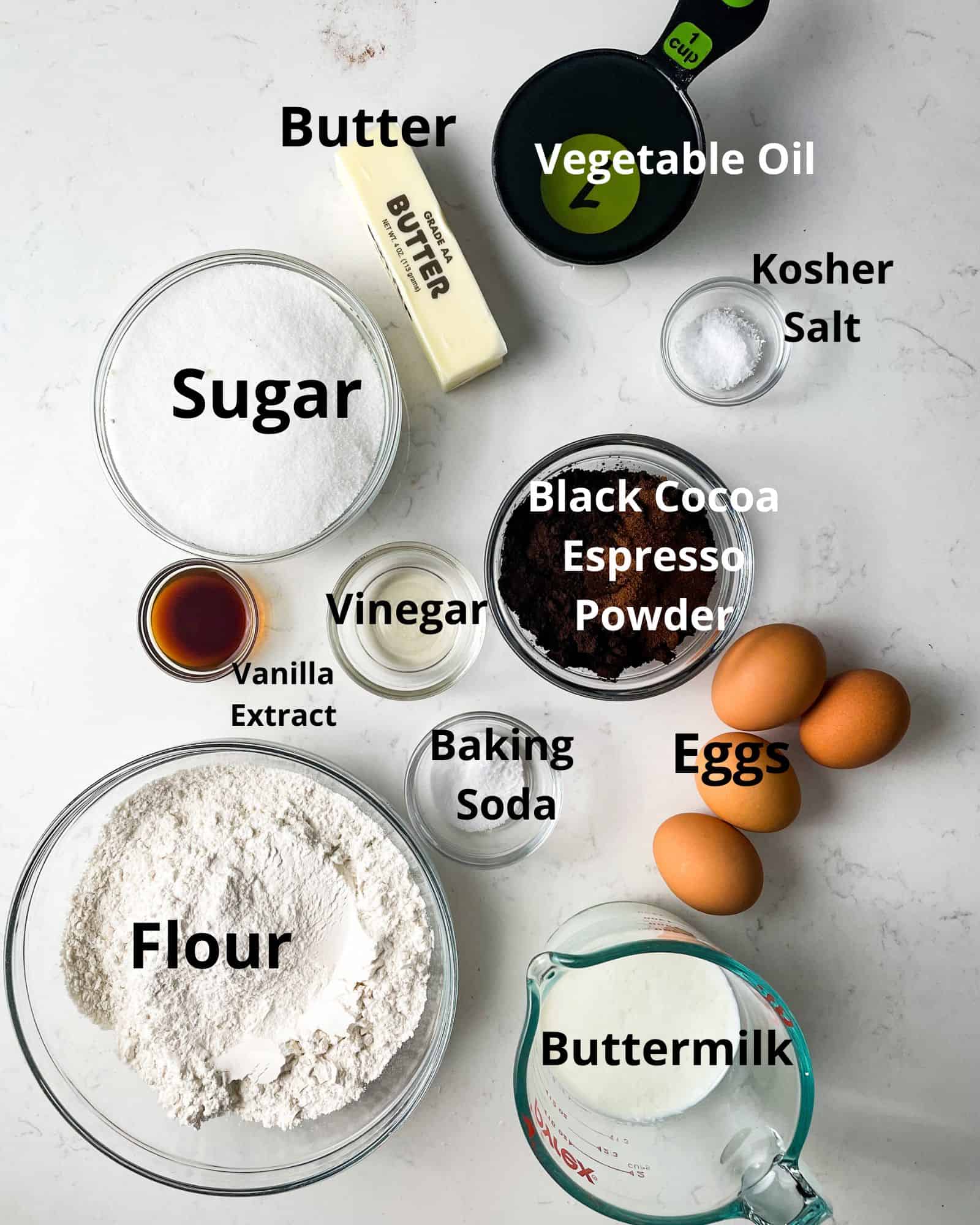 ingredients to make black velvet cake - flour, sugar, eggs, vanilla extract, black cocoa, espresso powder, baking soda, buttermilk, vinegar, vegetable oil, butter, and kosher salt.