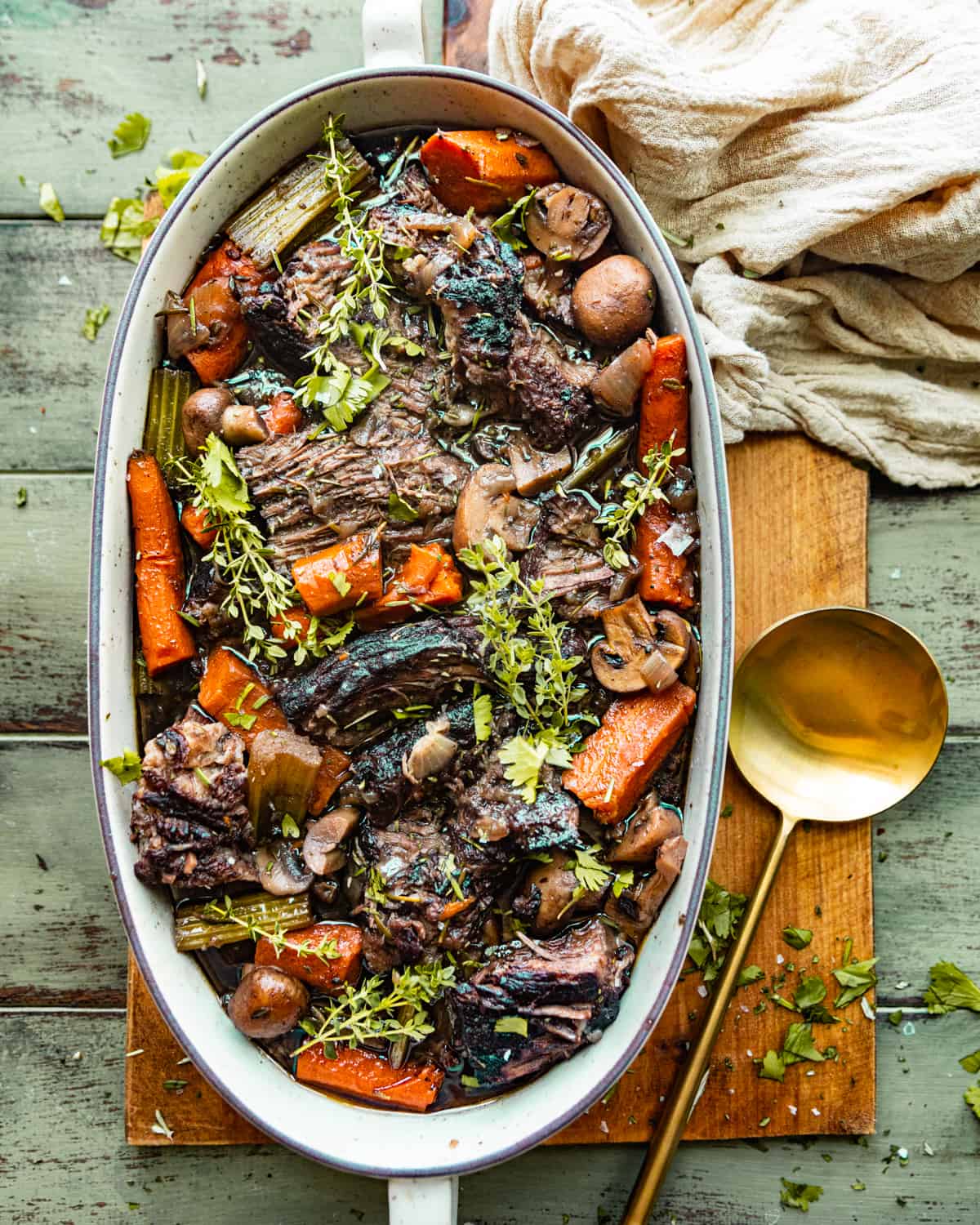 oven baked chuck roast in a serving dish with veggies and fresh herbs.