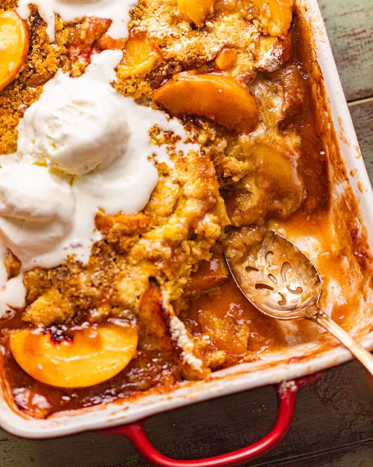 peach cobbler in a baking dish with a spoon.