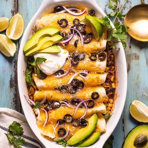 chicken enchiladas in a casserole dish garnished with sour cream, avocado, and olives.