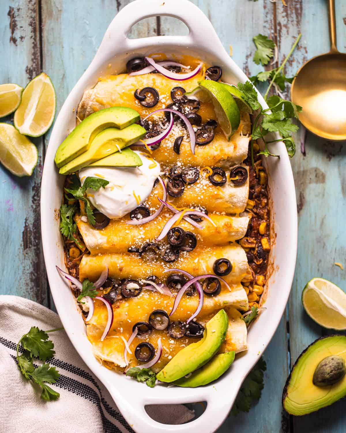 chicken enchiladas in a casserole dish garnished with sour cream, avocado, and olives.
