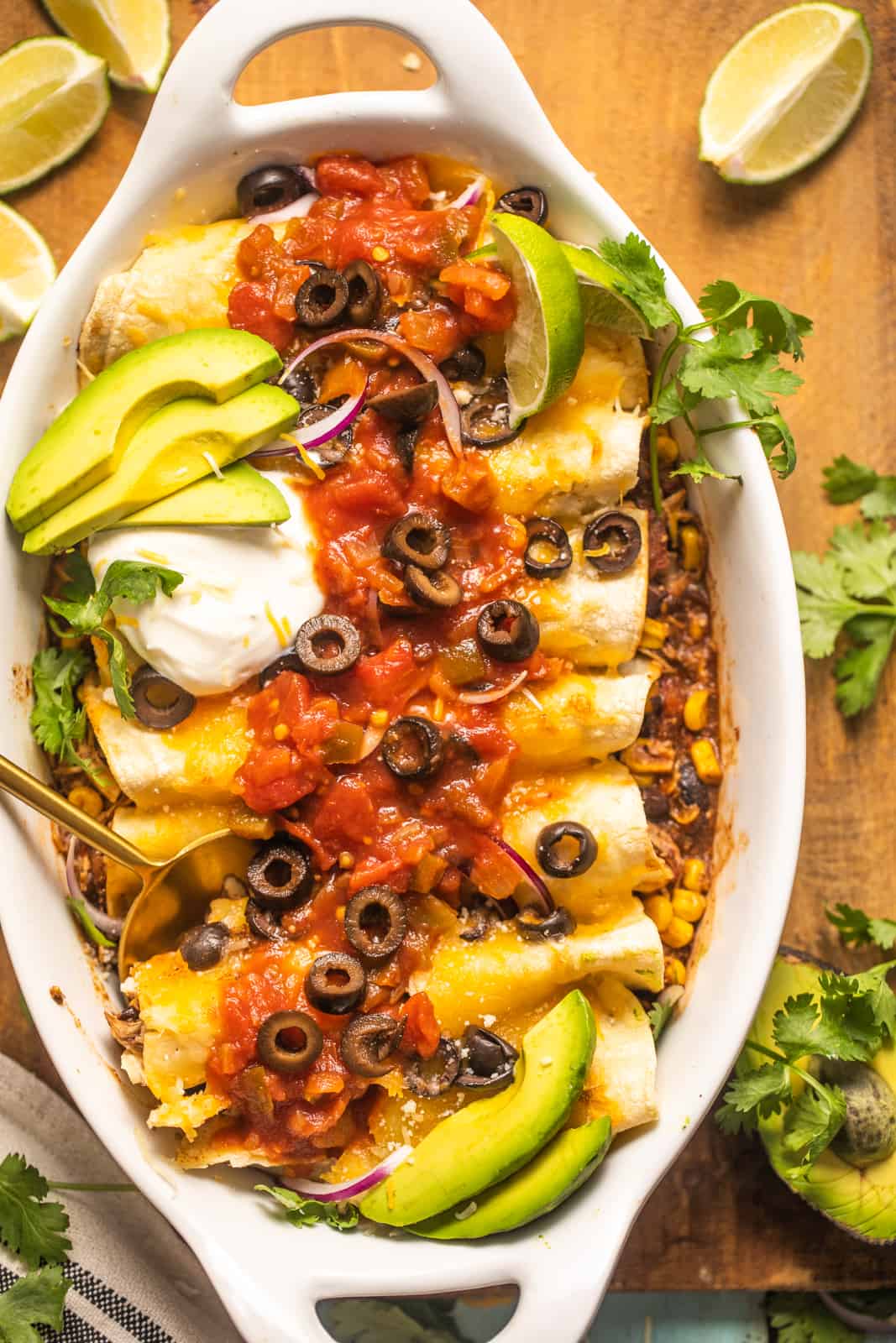 slow cooker chicken enchiladas in a casserole dish topped with salsa, sour cream, red onion, and avocado.