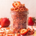 strawberry shortcake crumbles in a glass jar with strawberries on top.