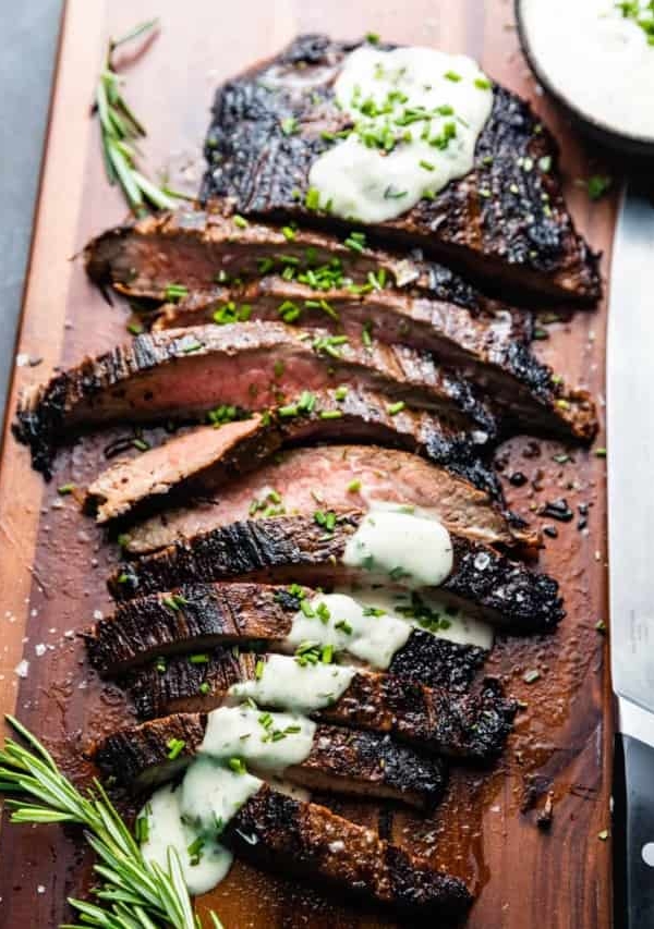 sliced bavette steak on a cutting board topped with garlic butter sauce.