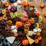 halloween charcuterie board on a table with mini pumpkins and skeleton hands.