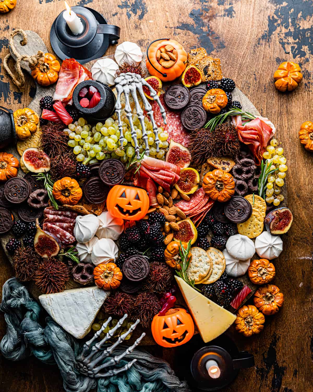 halloween charcuterie board on a table with mini pumpkins and skeleton hands.