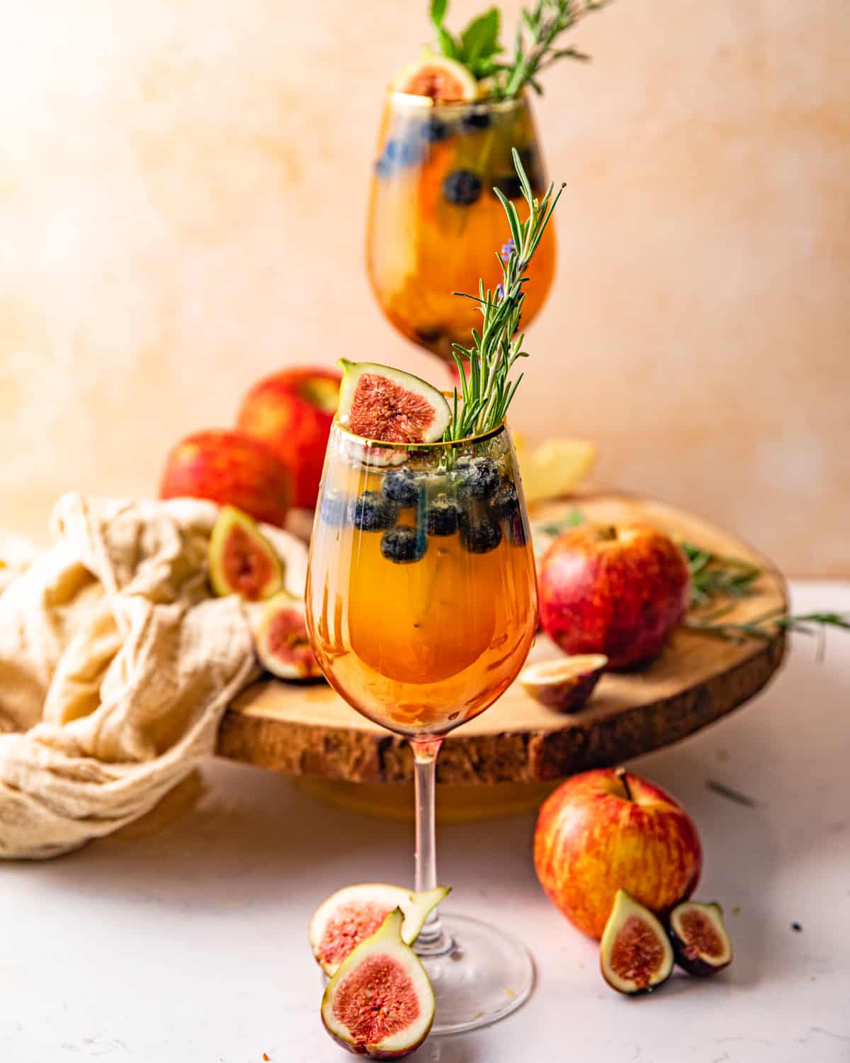 two glasses of white wine sangria garnished with fresh herbs, figs, and apples.