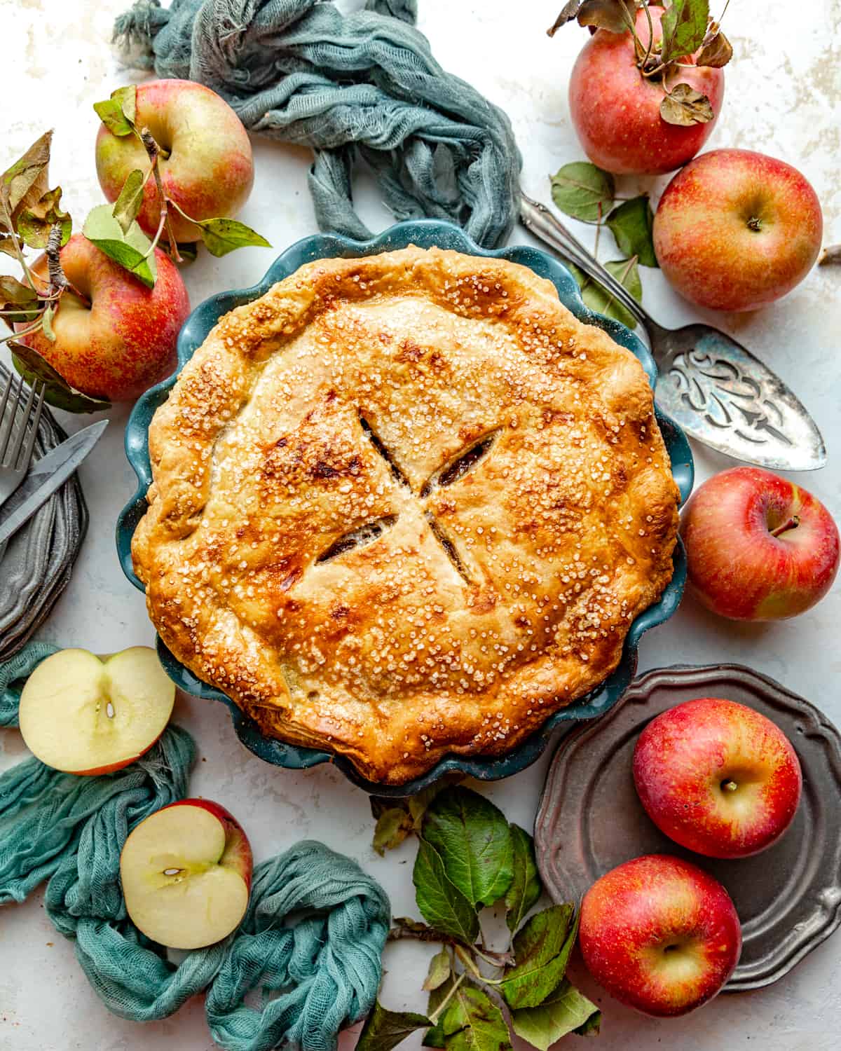 classic apple pie in a pie dish surrounded by apples.