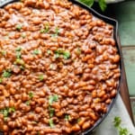 baked beans with ground beef in a skillet topped with sliced green onions.