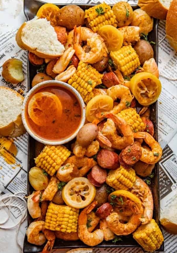 shrimp boil on a serving platter with drawn butter and sliced bread.