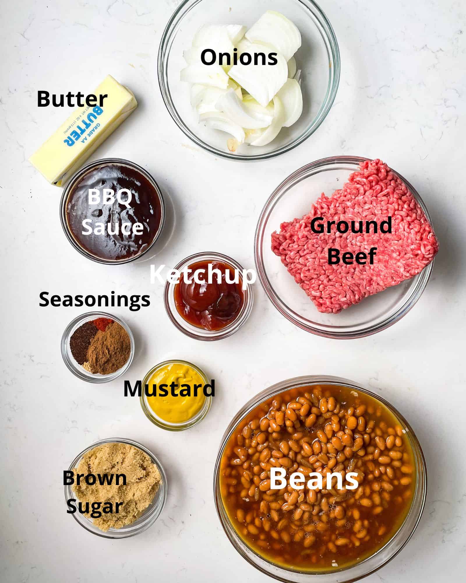 ingredients to make baked beans - canned beans, ground beef, onions, butter, bbq sauce, ketchup, mustard, seasonings, and brown sugar.