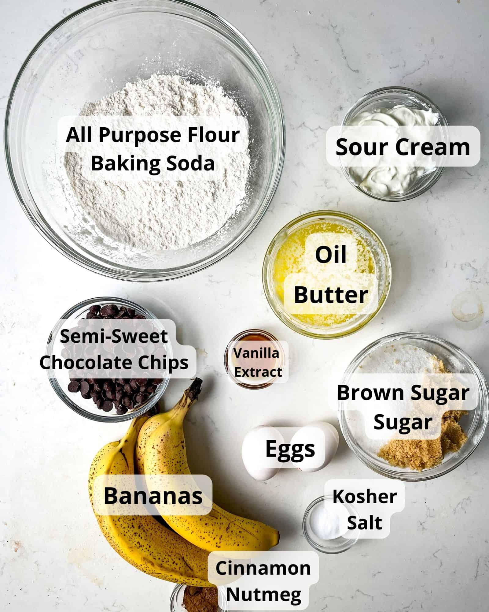 ingredients to make chocolate chip banana bread - all purpose flour, baking soda, kosher salt, oil, butter, sour cream, bananas, eggs, brown sugar, sugar, cinnamon, nutmeg, melted butter. and chocolate chips.