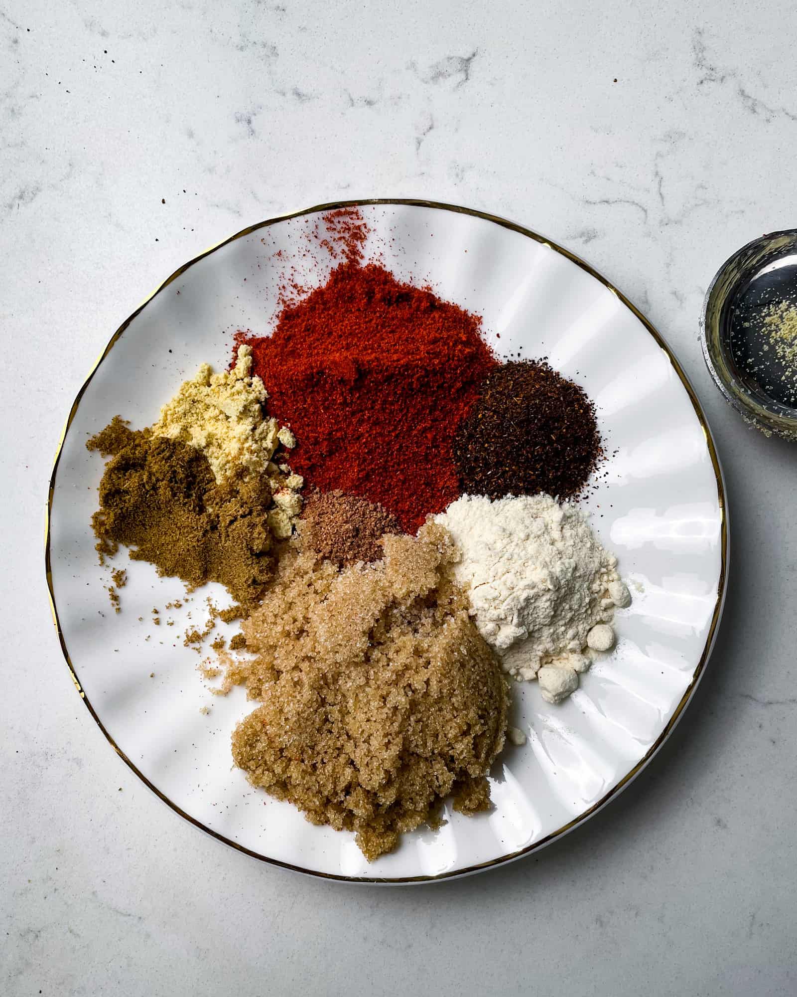 the dry rub ingredients on a plate - smoked paprika, black pepper, onion powder, ground mustard, onion powder, chili powder, coriander, and brown sugar.