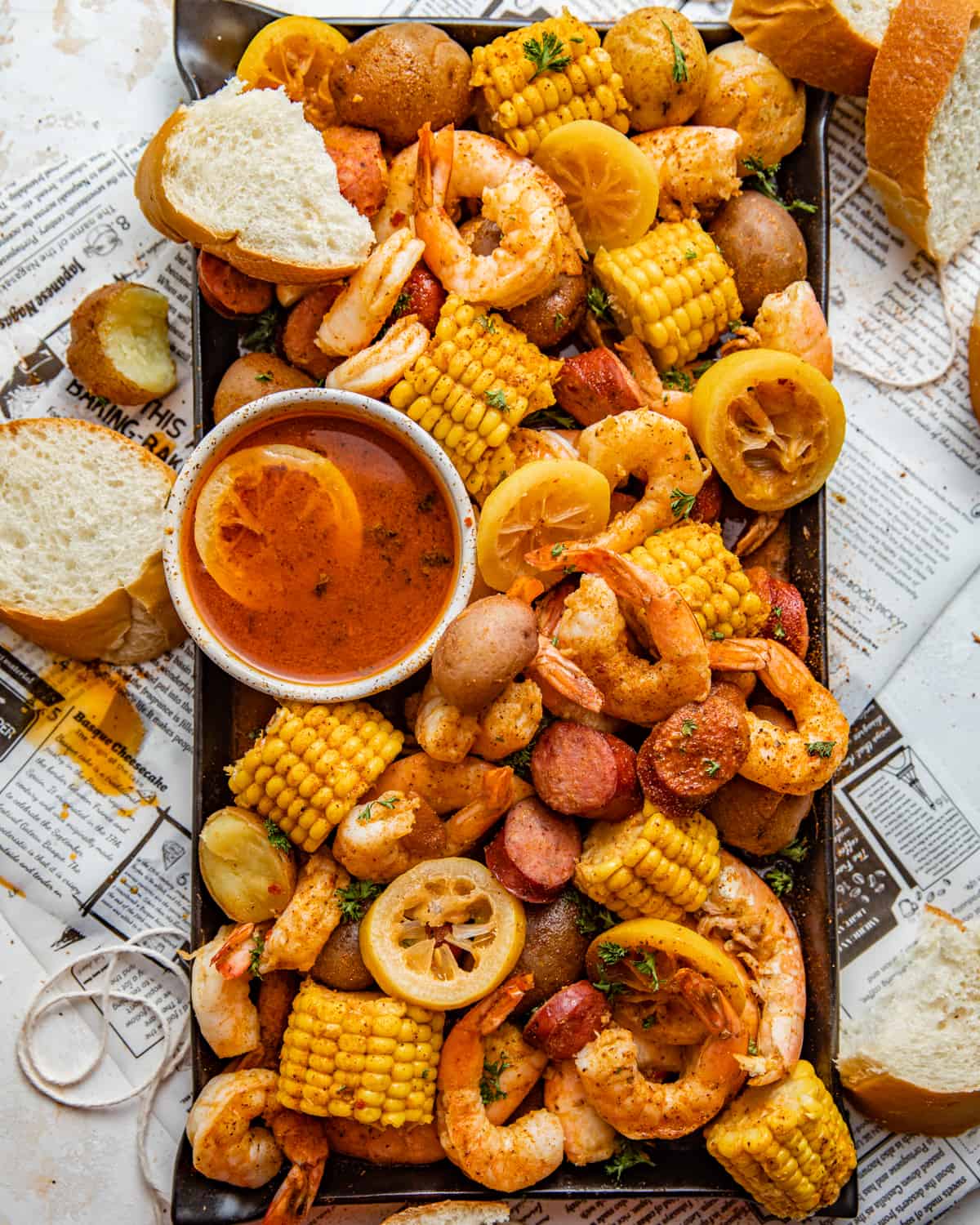 shrimp boil on a serving platter with drawn butter and sliced bread.