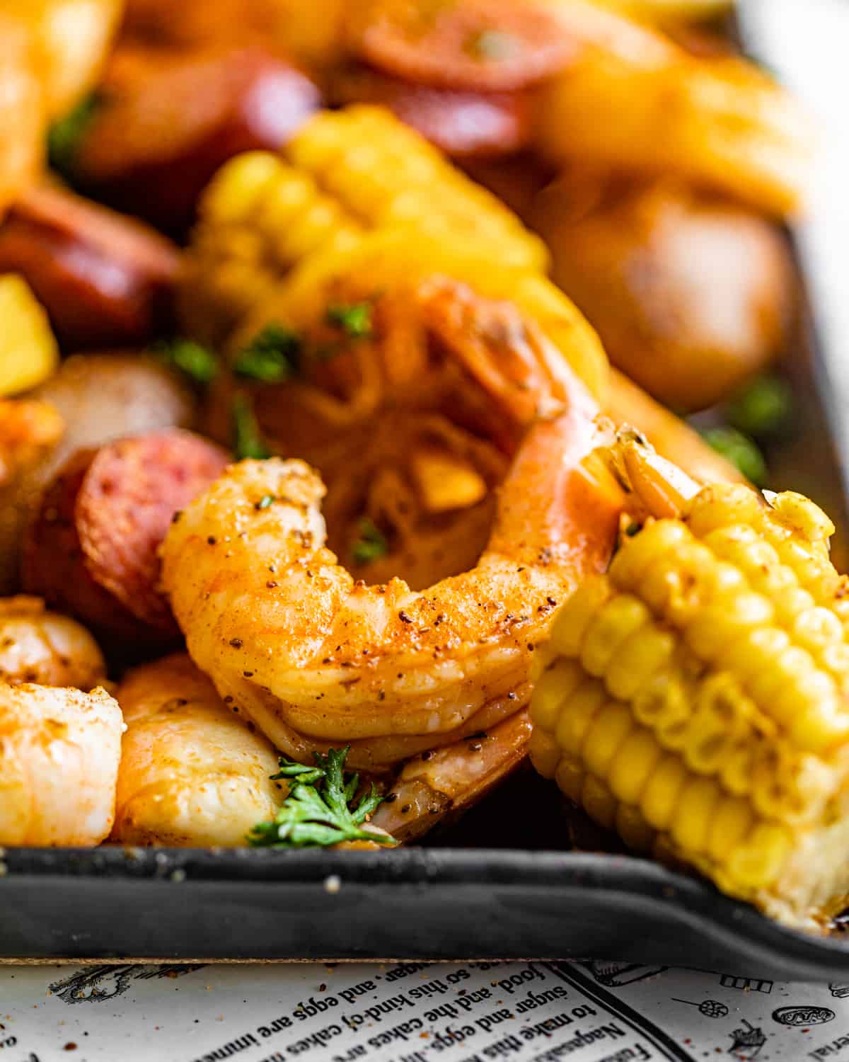 a piece of shrimp on a plate with corn, sausage, and potatoes.
