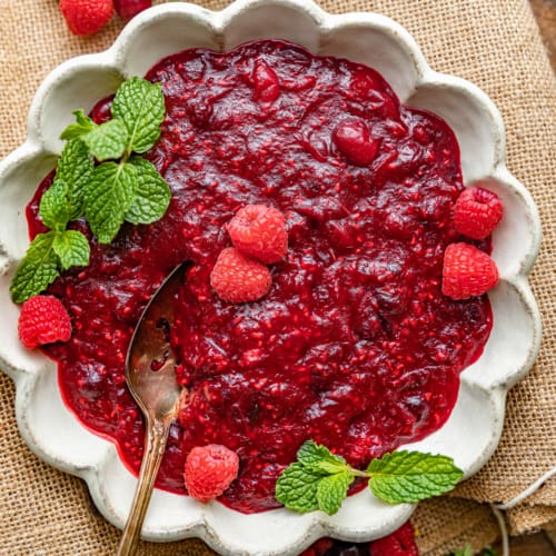 cranberry raspberry sauce in a bowl topped with fresh raspberries.