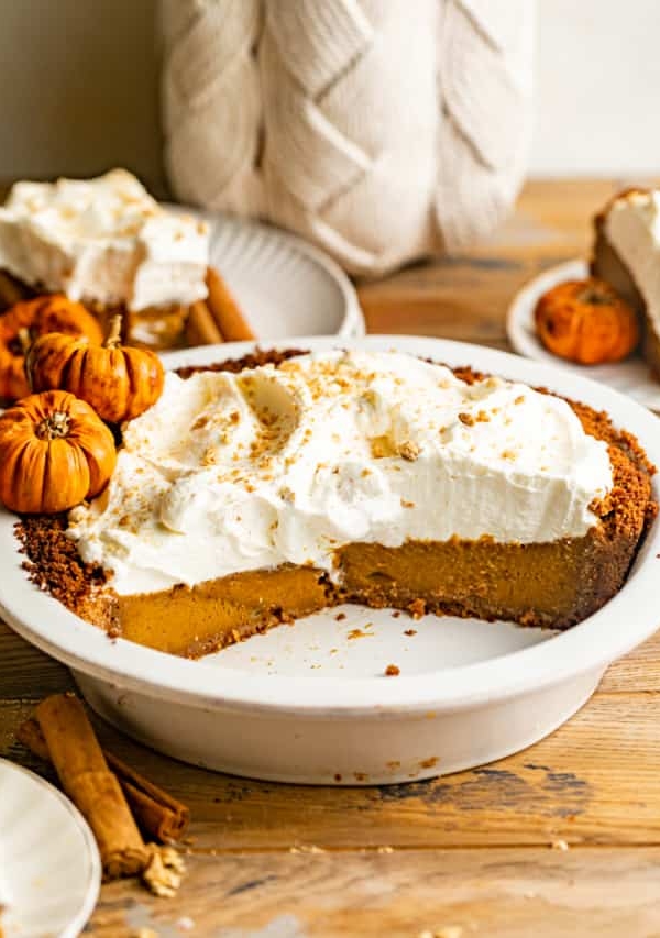 pumpkin pie with graham cracker crust in a pie dish topped with whipped cream.