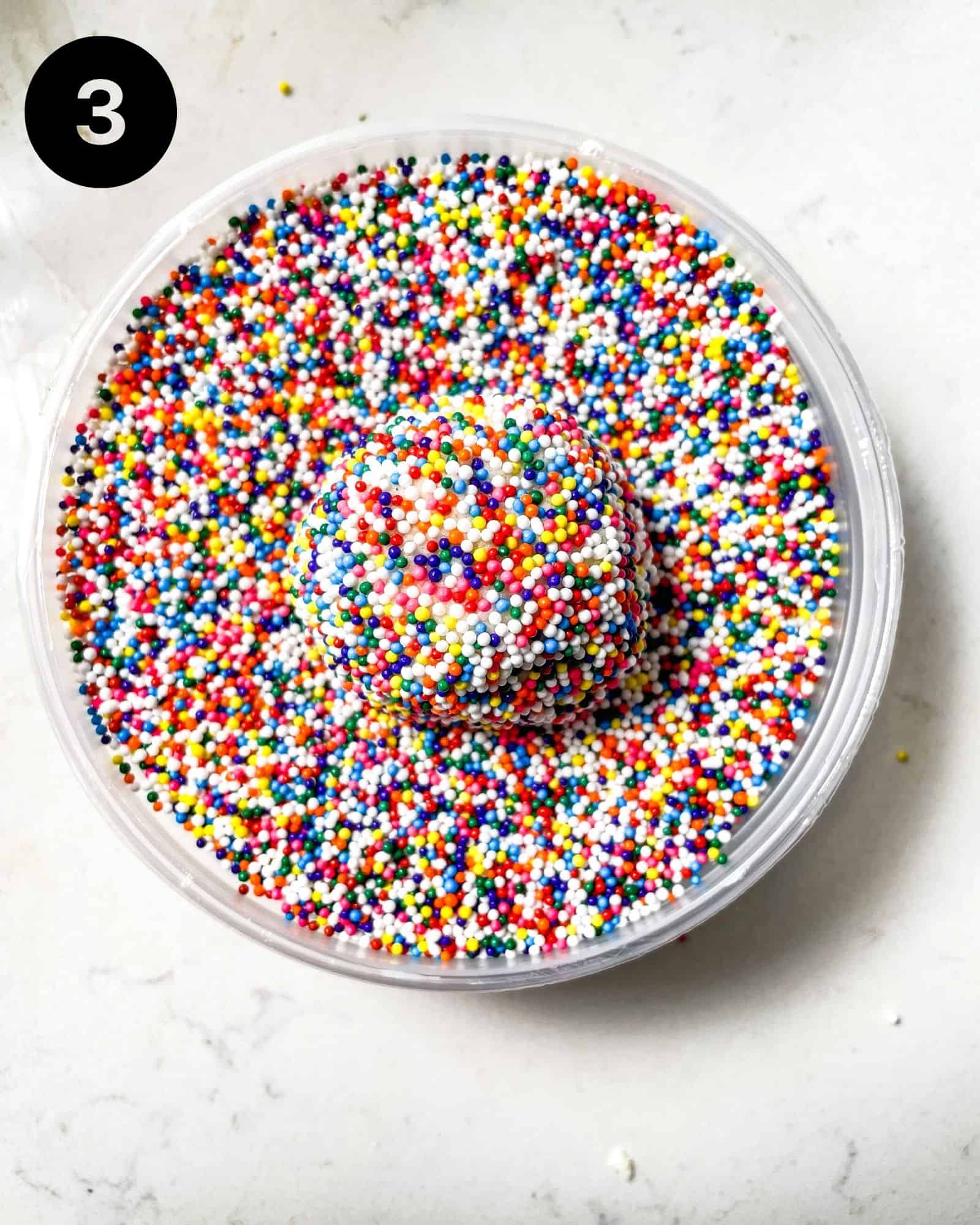 a cookie dough ball in a bowl of sprinkles.