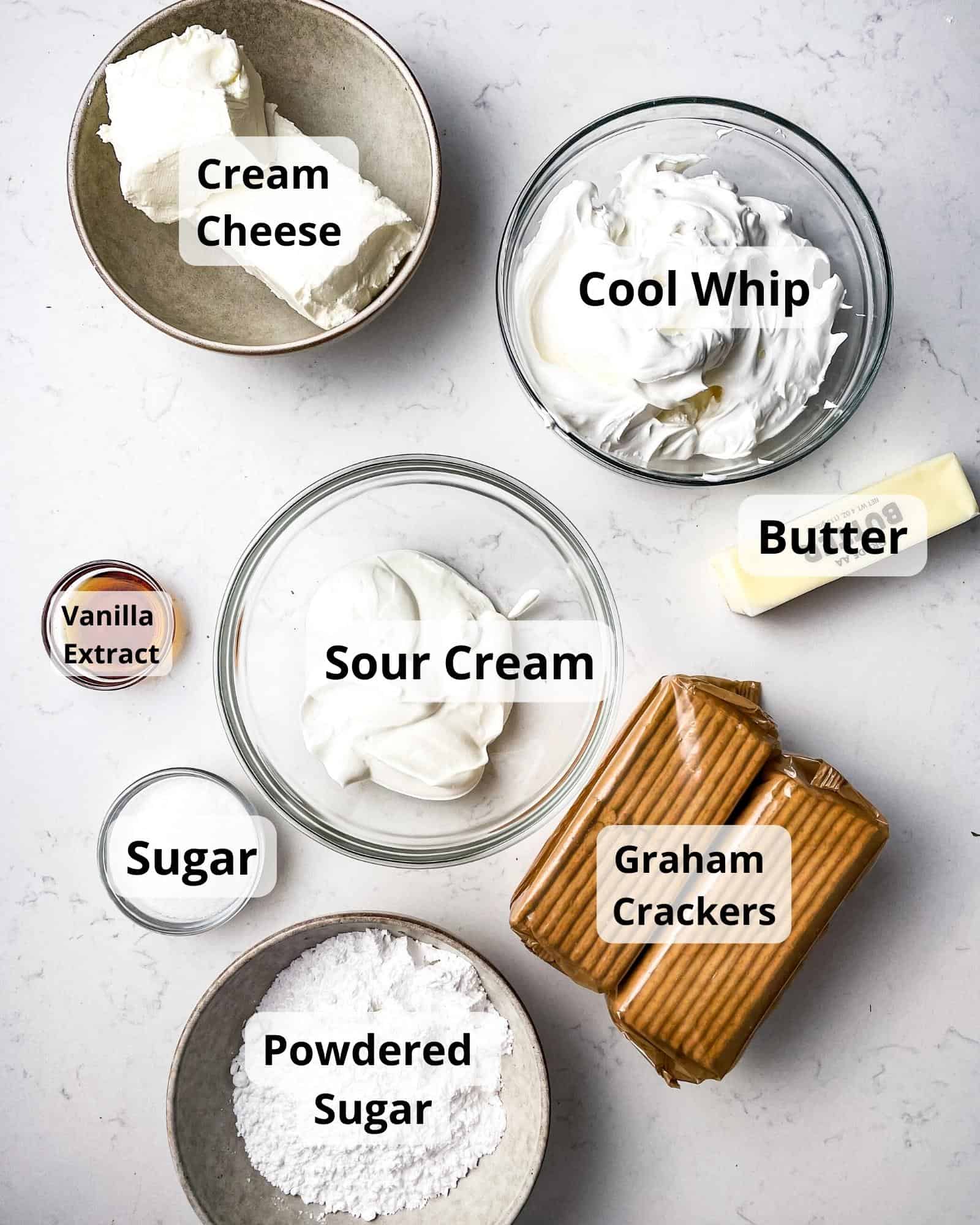 ingredients to make philadelphia no bake cheesecake - cream cheese, cool whip, sour cream, butter, vanilla extract, graham crackers, butter, powdered sugar, and sugar.