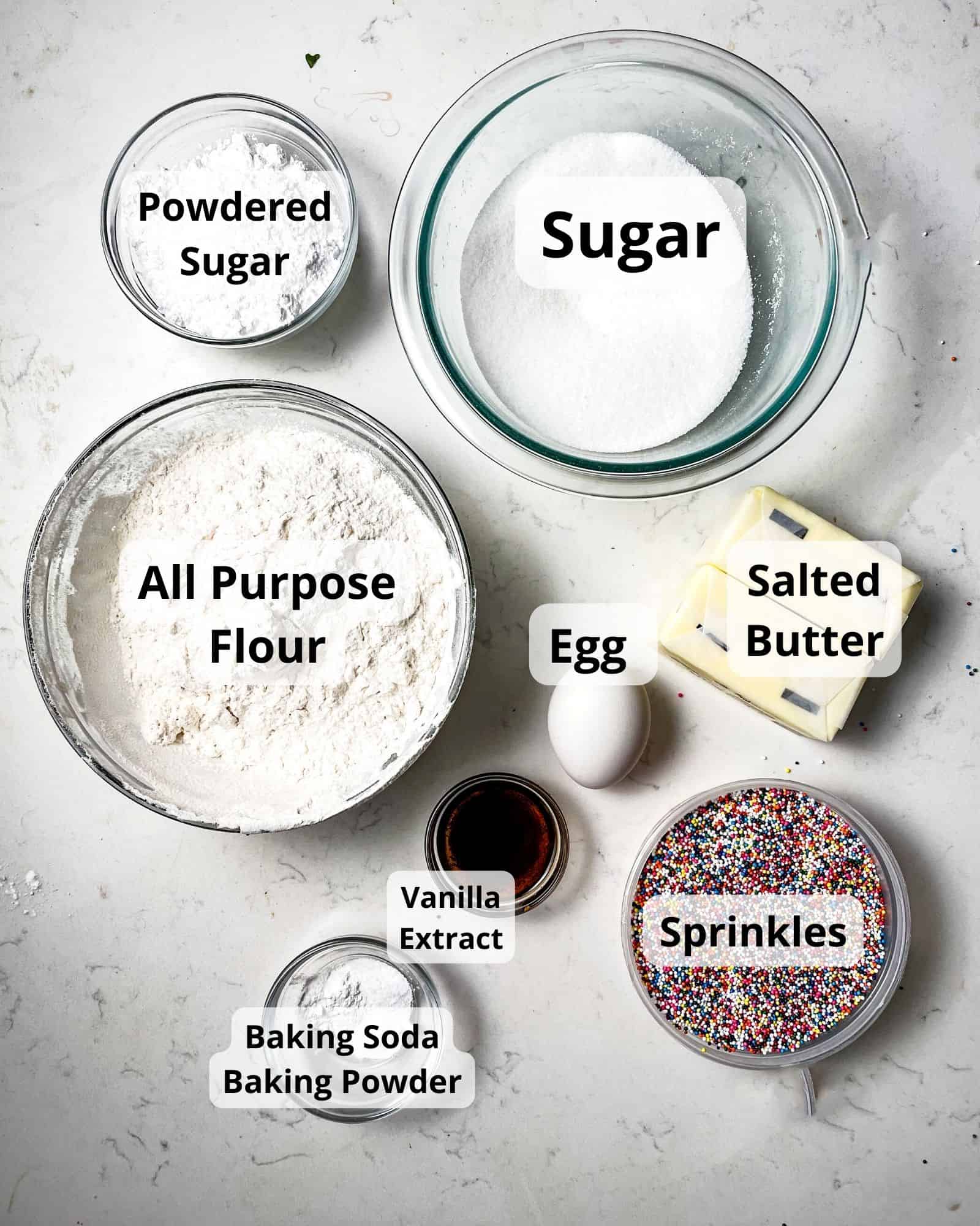 ingredients to make sprinkle sugar cookies - powdered sugar, sugar, all purpose flour, egg, salted butter, baking soda, baking powder, vanilla extract, and sprinkles.