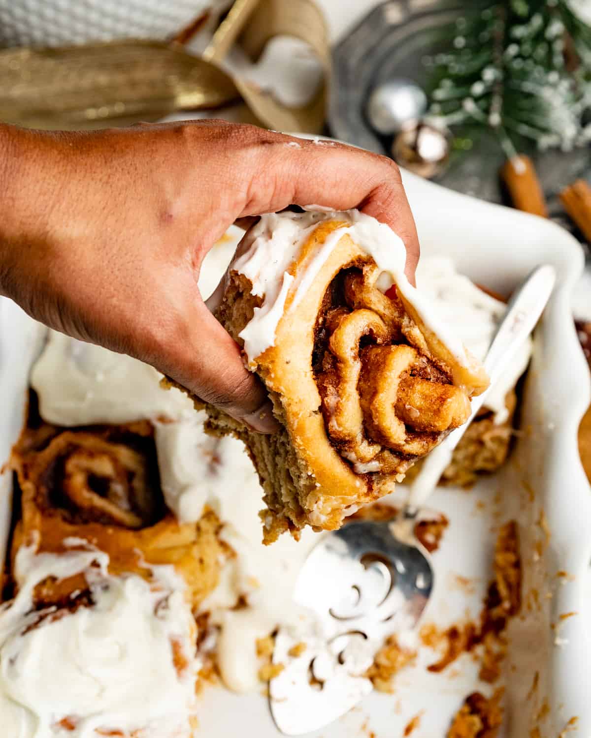a hand holding a cinnamon roll over top of a baking dish.