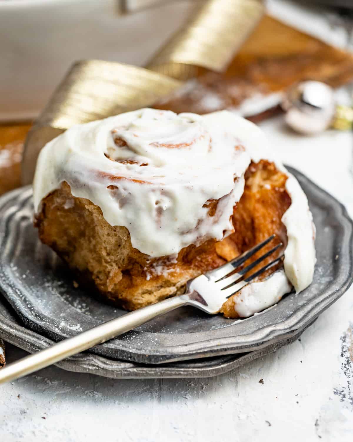 a gooey cinnamon bun on a plate with a fork covered in frosting.