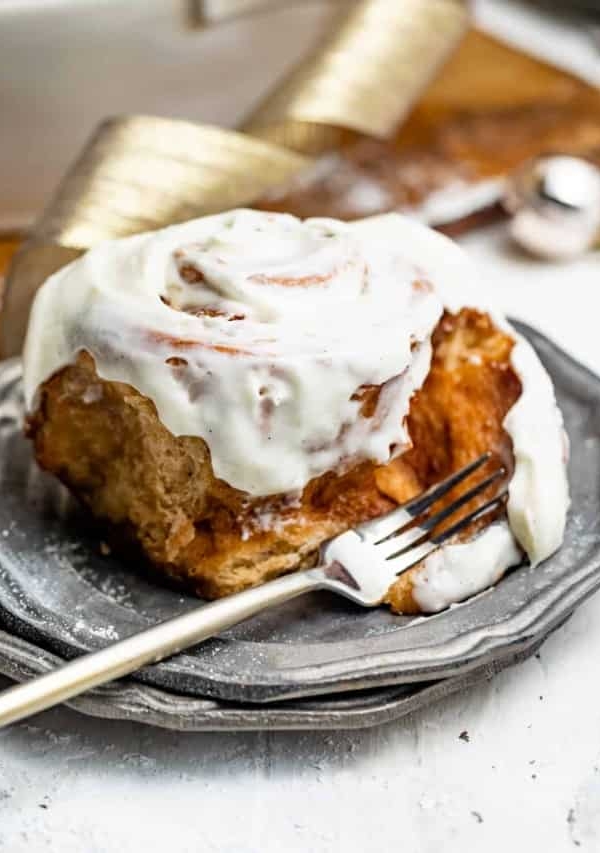 a gooey cinnamon bun on a plate with a fork covered in frosting.