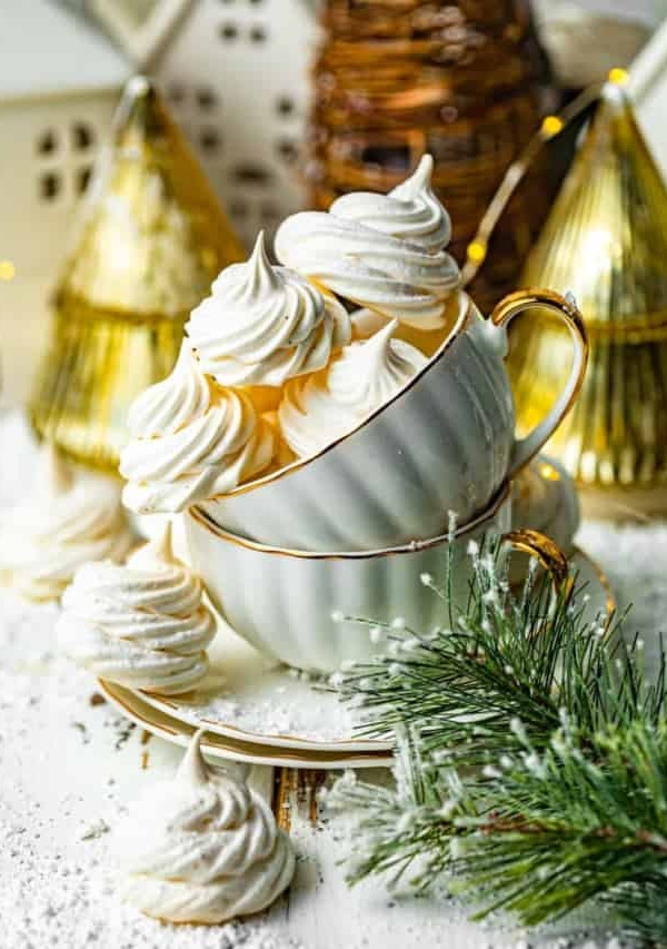 meringue cookies in a tea cup in front of a gold christmas tree.