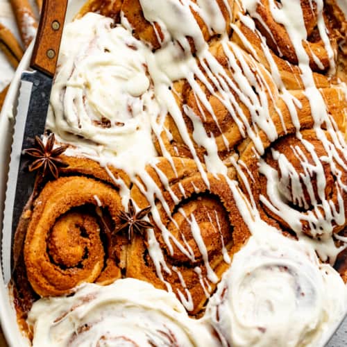 cinnamon rolls in a baking dish covered in a cream cheese icing.