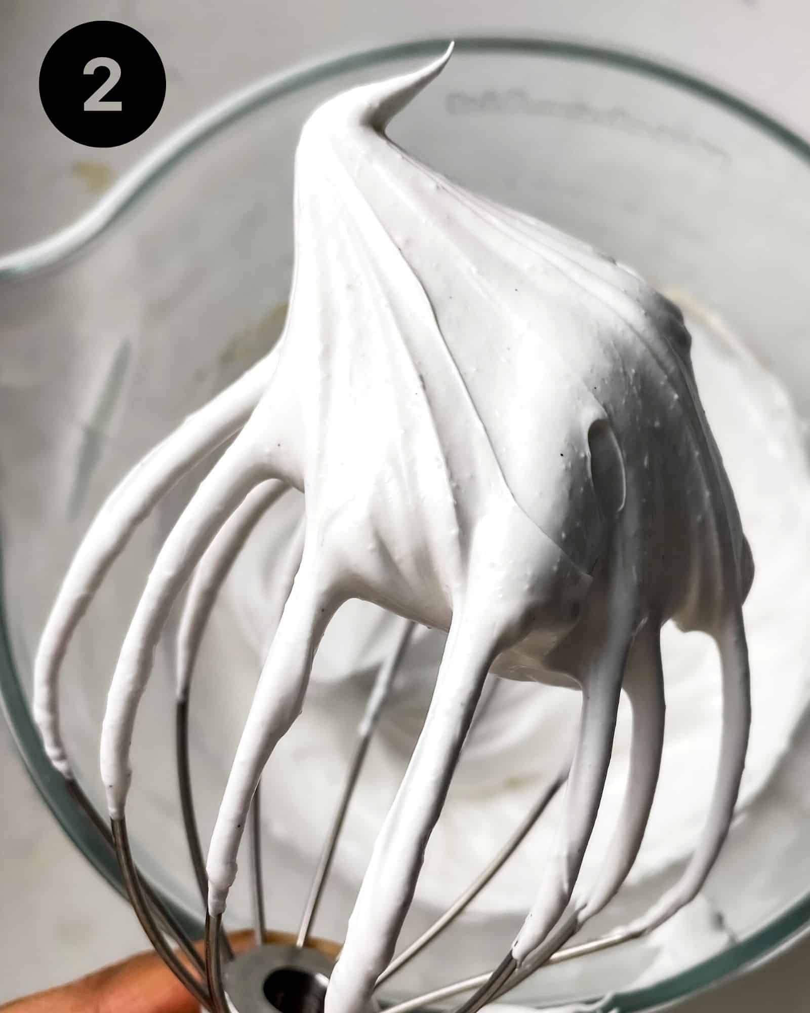 meringue on a whisk showing stiff peaks.