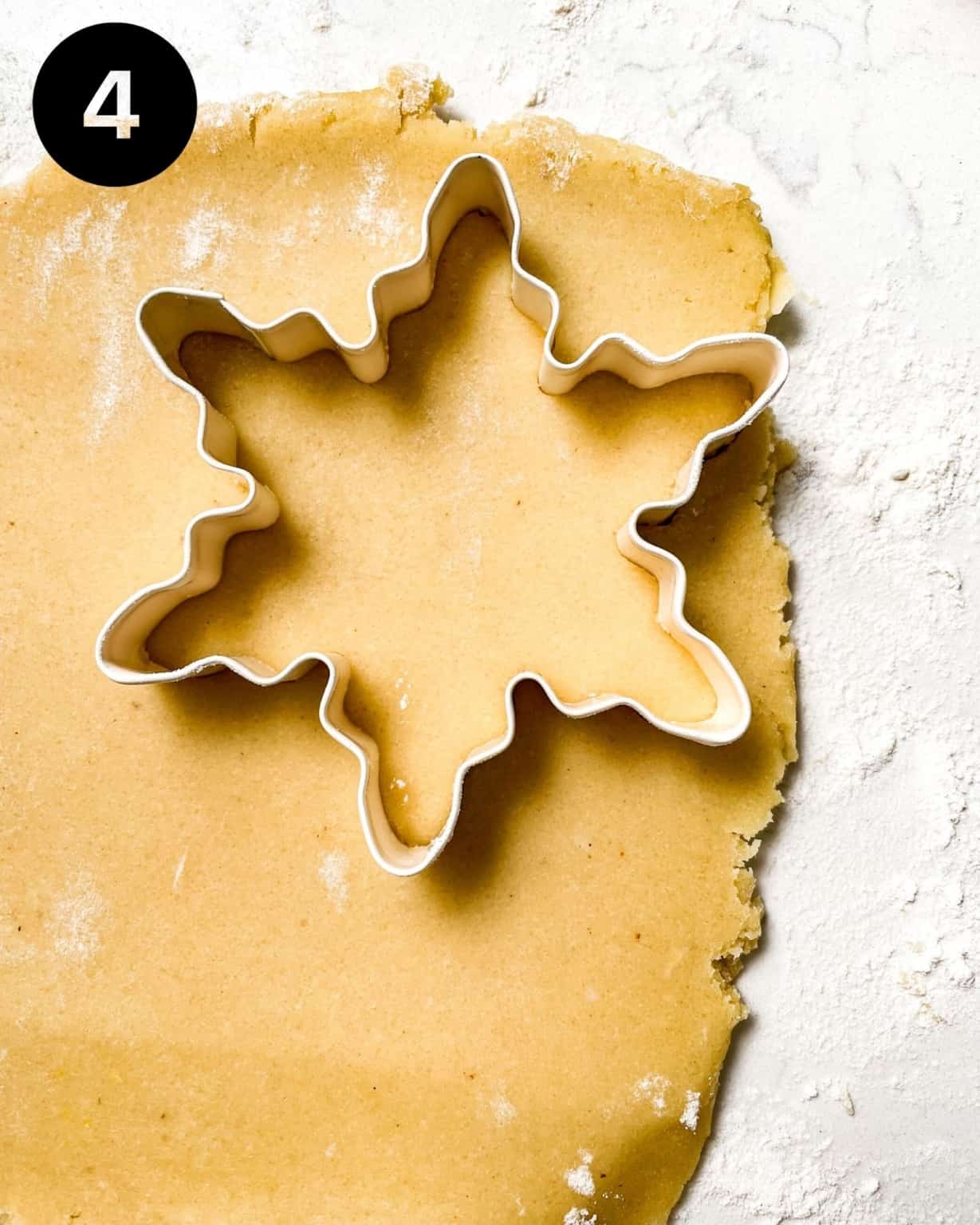 cookie dough rolled out onto a surface with a snowflake cookie cutter pressed into the dough.