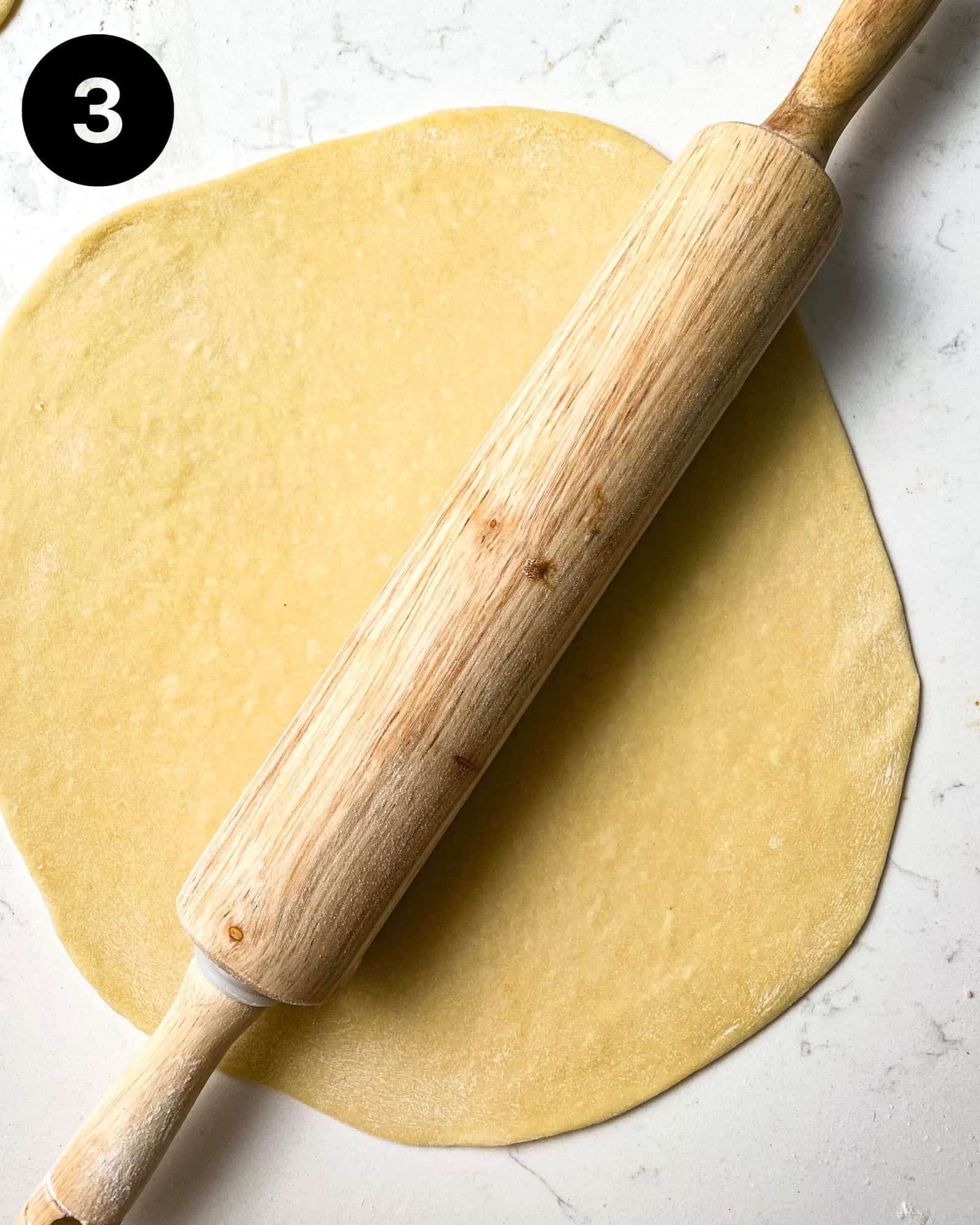 a rolling pin on top of a large piece of rolled out dough on a floured surface.