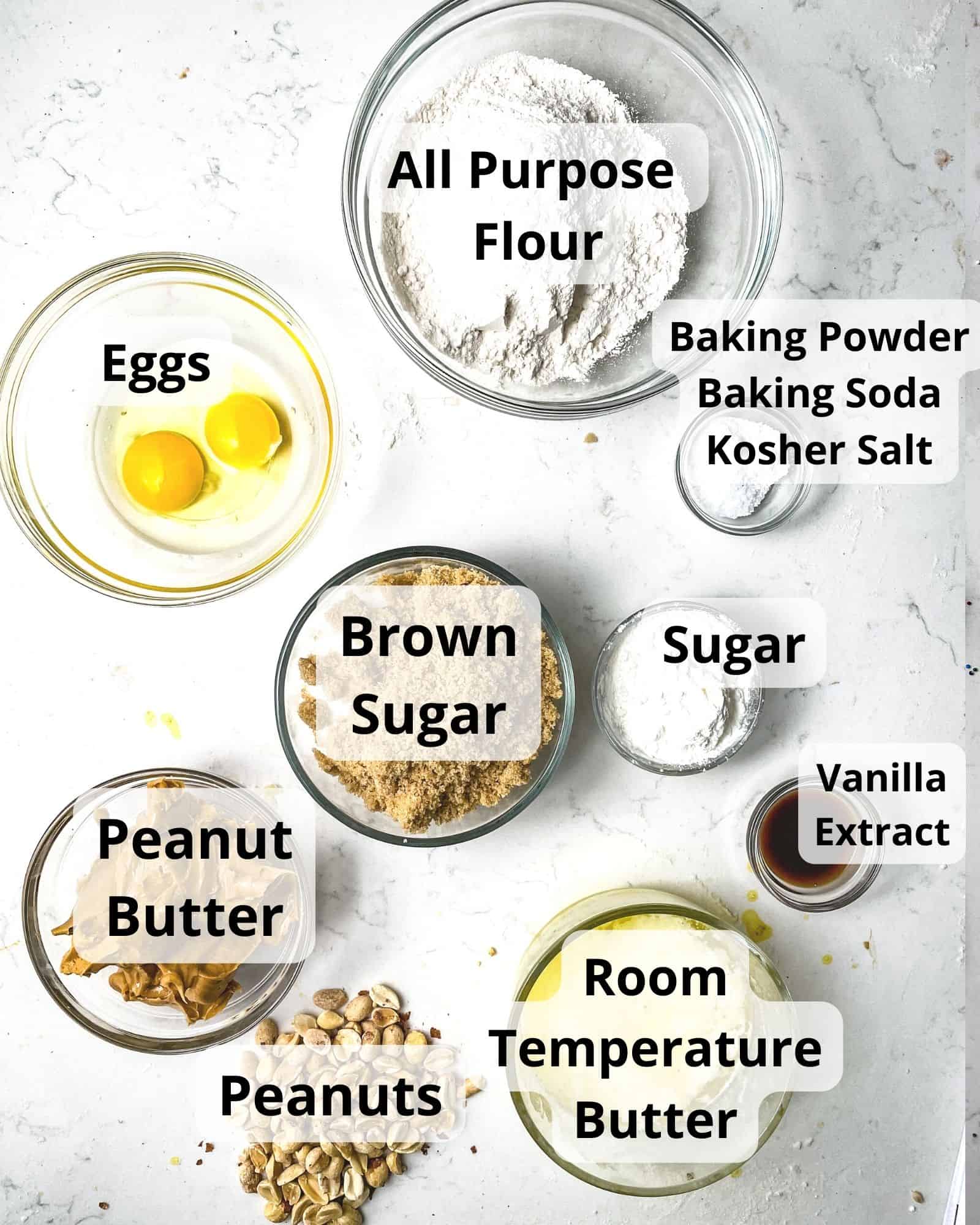 ingredients to make chewy peanut butter cookies - flour, butter, baking soda, baking powder, brown sugar, sugar, eggs, vanilla extract, peanut butter, salt, and chopped peanuts.