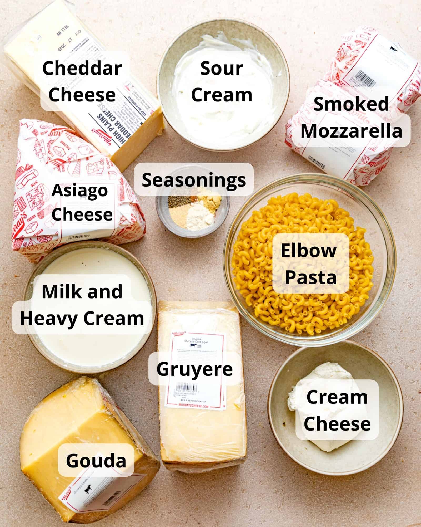 ingredients to make mac and cheese - cheddar cheese, asiago, smoked mozzarella, cheddar cheese, elbow pasta, sour cream, milk, heavy cream, cream cheese, gouda, gruyere, and seasonings.