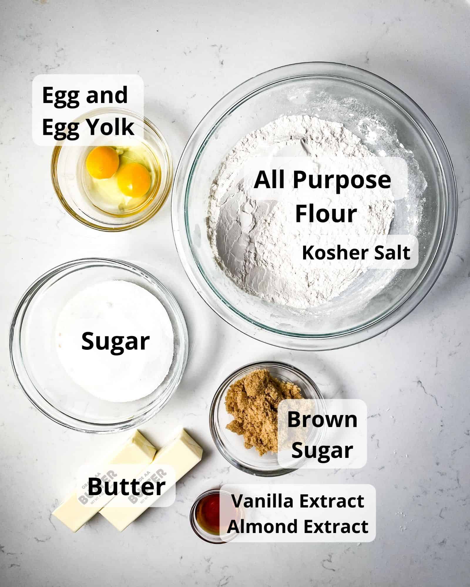 ingredients to make snowflake cookies - flour, salt, egg, egg yolk, sugar, brown sugar, vanilla extract, almond extract, and butter.