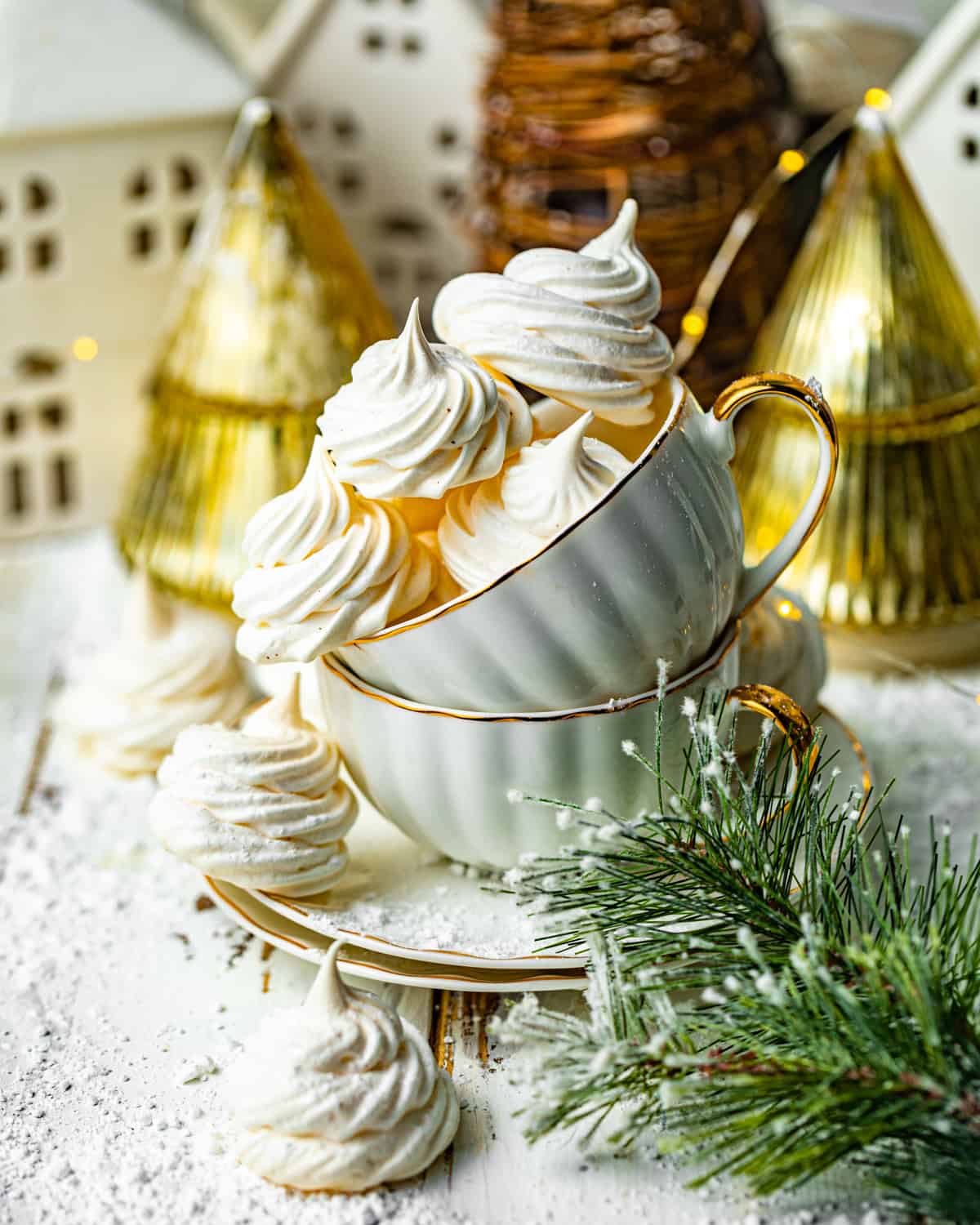 meringue cookies in a tea cup in front of a gold christmas tree.