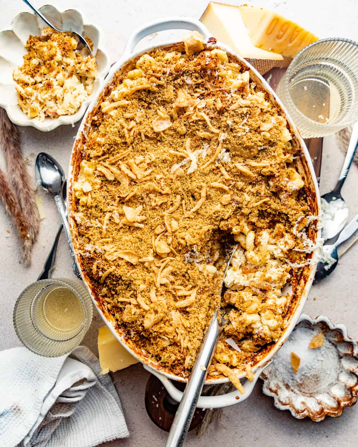 prosciutto mac and cheese in a baking dish surrounded by cheeses, spoons, and glasses.