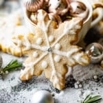 a snowflake cookies in front of a tea cup filled with christmas ornaments.