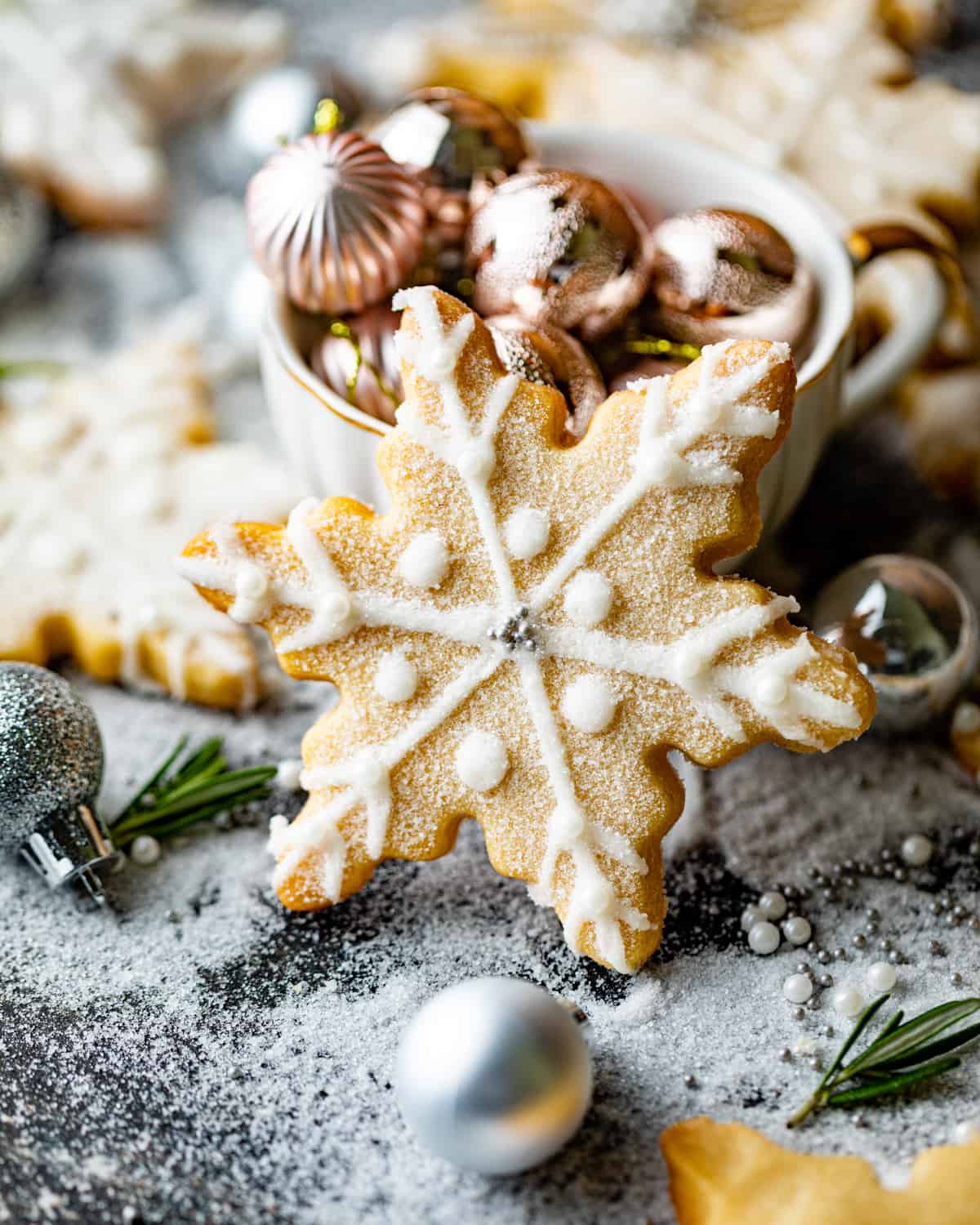 a snowflake cookie standing up on a table with christmas bulbs around the cookie.