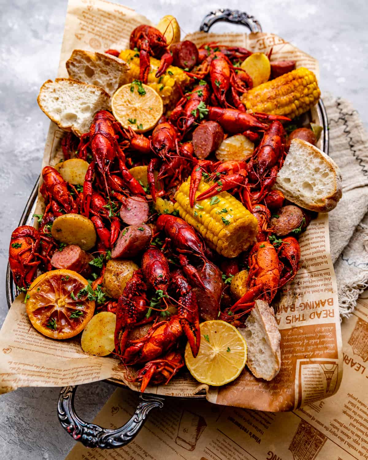 crawfish, corn, potatoes, and sausage on a large tray with fresh bread garnished with parsley.