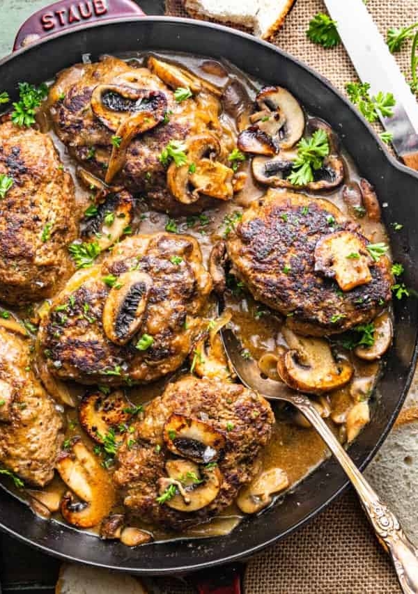 salisbury steaks in a pan with onion gravy garnished with chopped parsley.