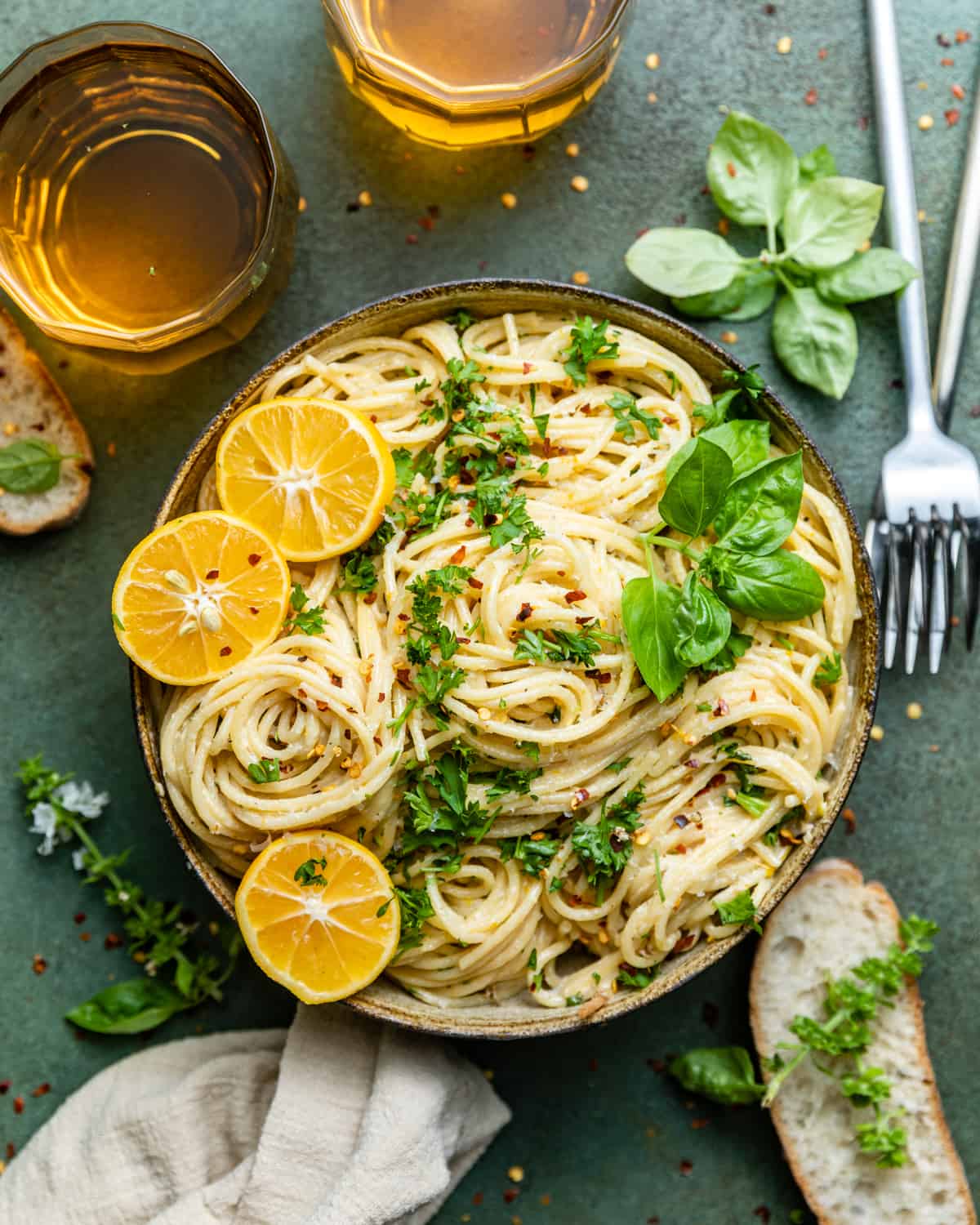 lemon garlic pasta in a bowl with lemons, basil, and chopped parsley on top.