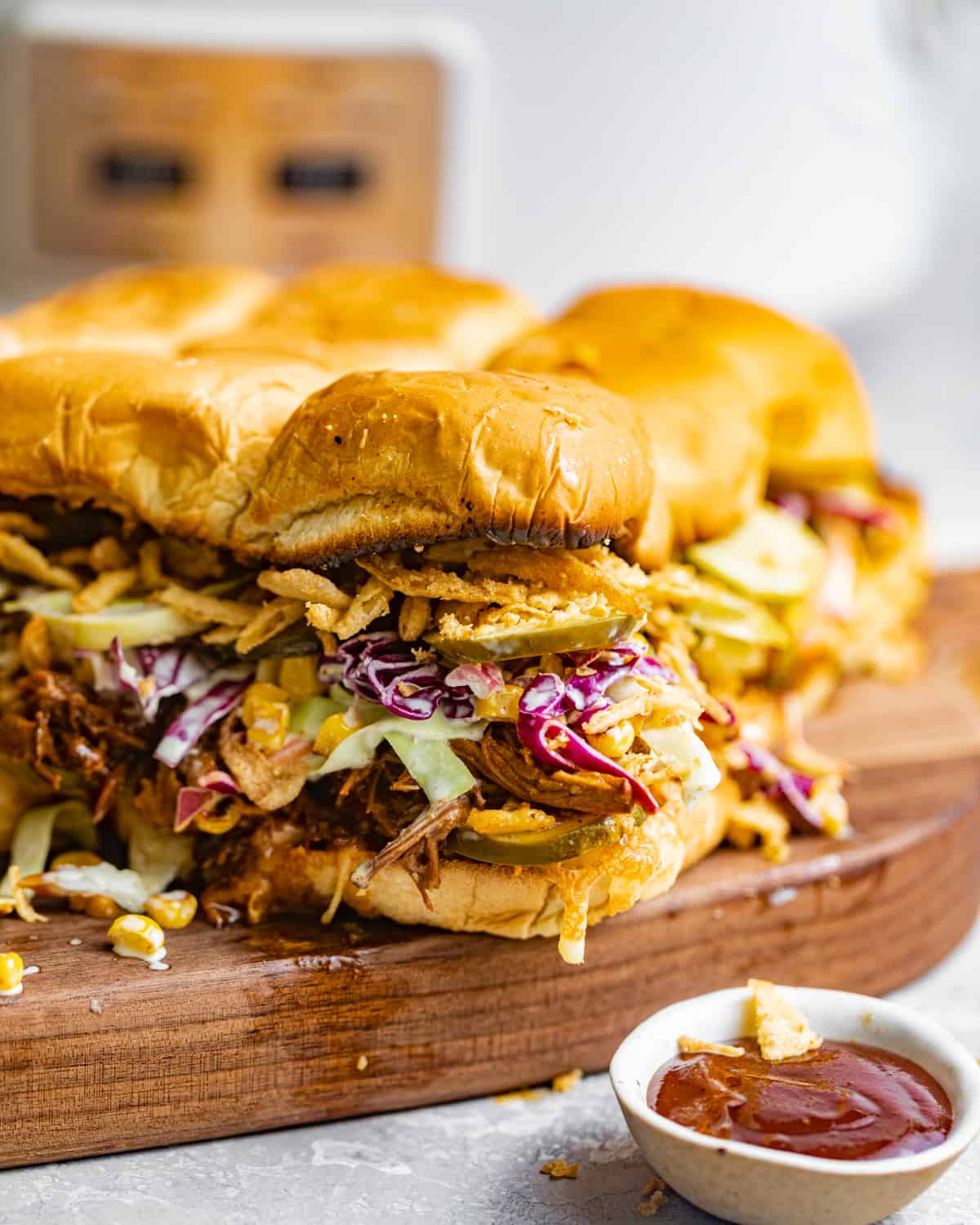 pulled pork sliders on a serving board in front of a white crockpot slow cooker.