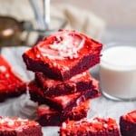 red velvet brownies stacked on top of each other next to a glass of milk.