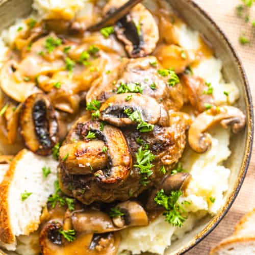 a bowl with mashed potatoes, salisbury steak, and mushroom gravy with a spoon.