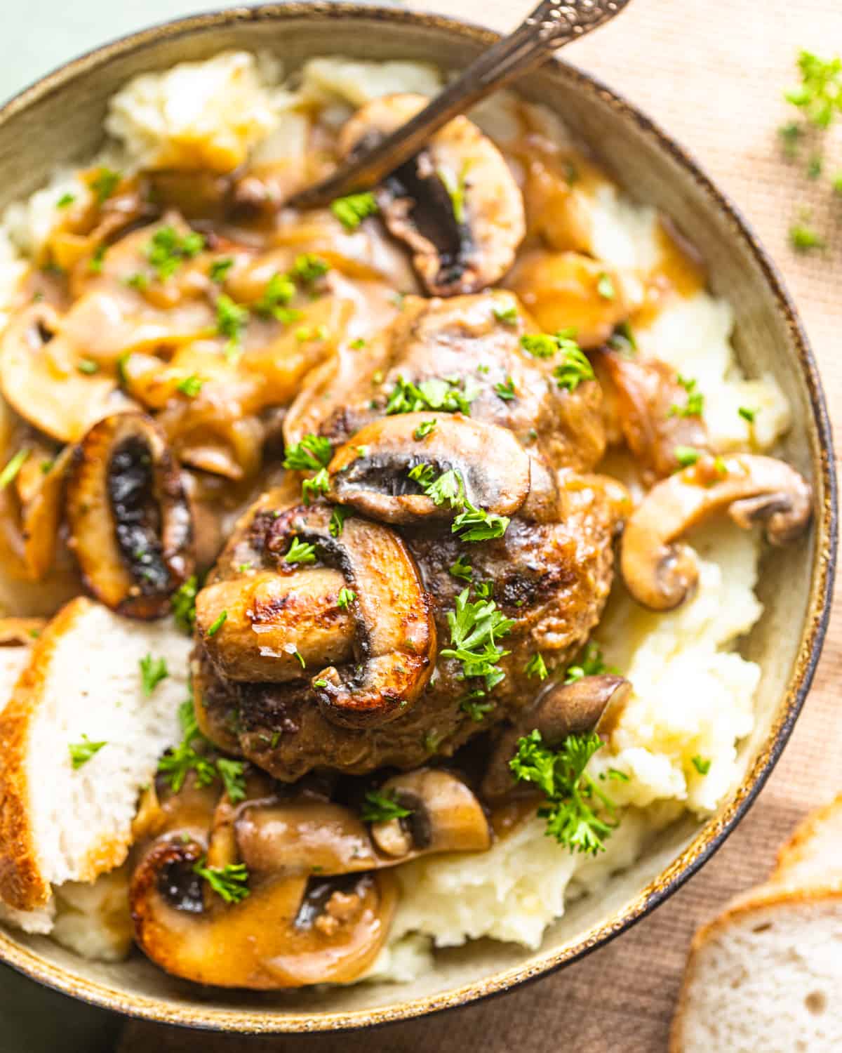 a bowl with mashed potatoes, salisbury steak, and mushroom gravy with a spoon.
