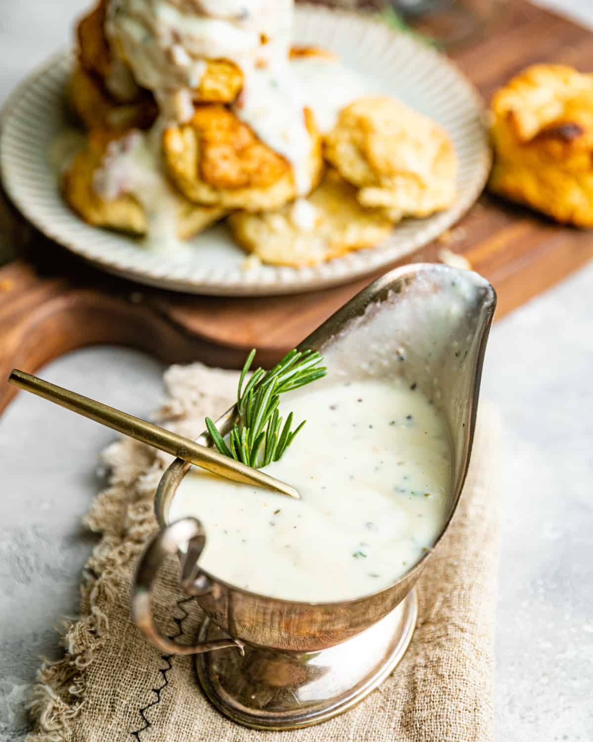 up close photo of white gravy in a gravy boat garnished with rosemary.
